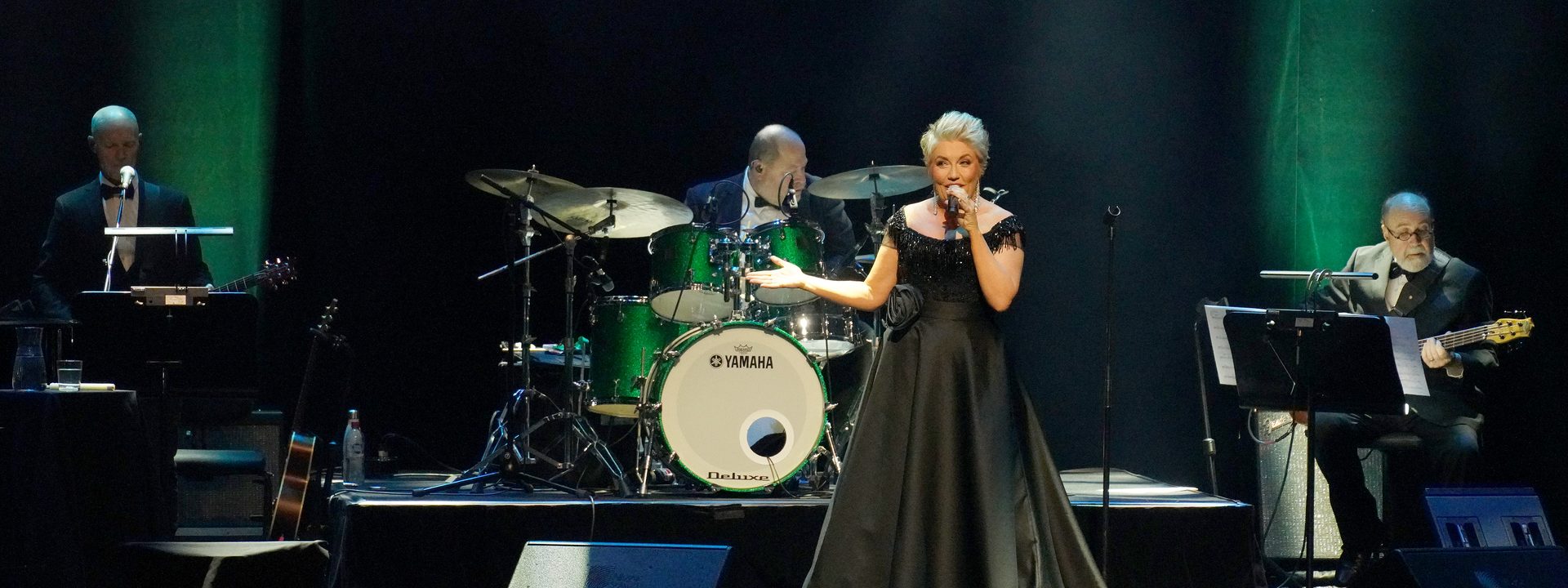 Melinda Schneider: The Way We Were - Female vocalist in a black dress performing centre stage with a live band under green theatrical lighting.