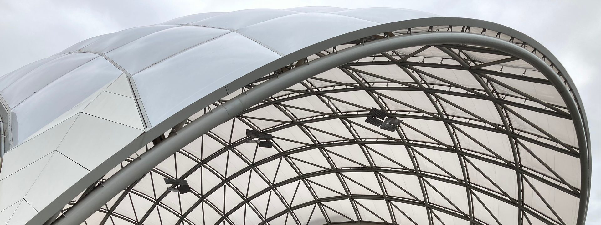 Adelaide Entertainment Centre - Modern curved building with geometric lattice roof structure and red entrance facade beneath overcast sky.