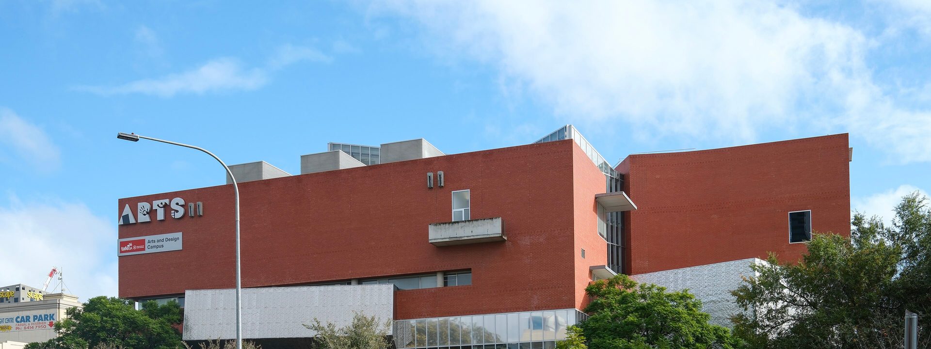 Adelaide College of the Arts - A modern red brick arts building with white sections sits on a corner street with green landscaping and street lamp.