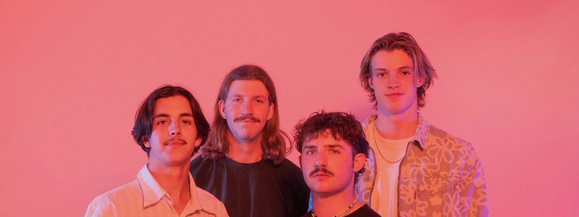 Four band members posed together against a pink-lit background for DICE.