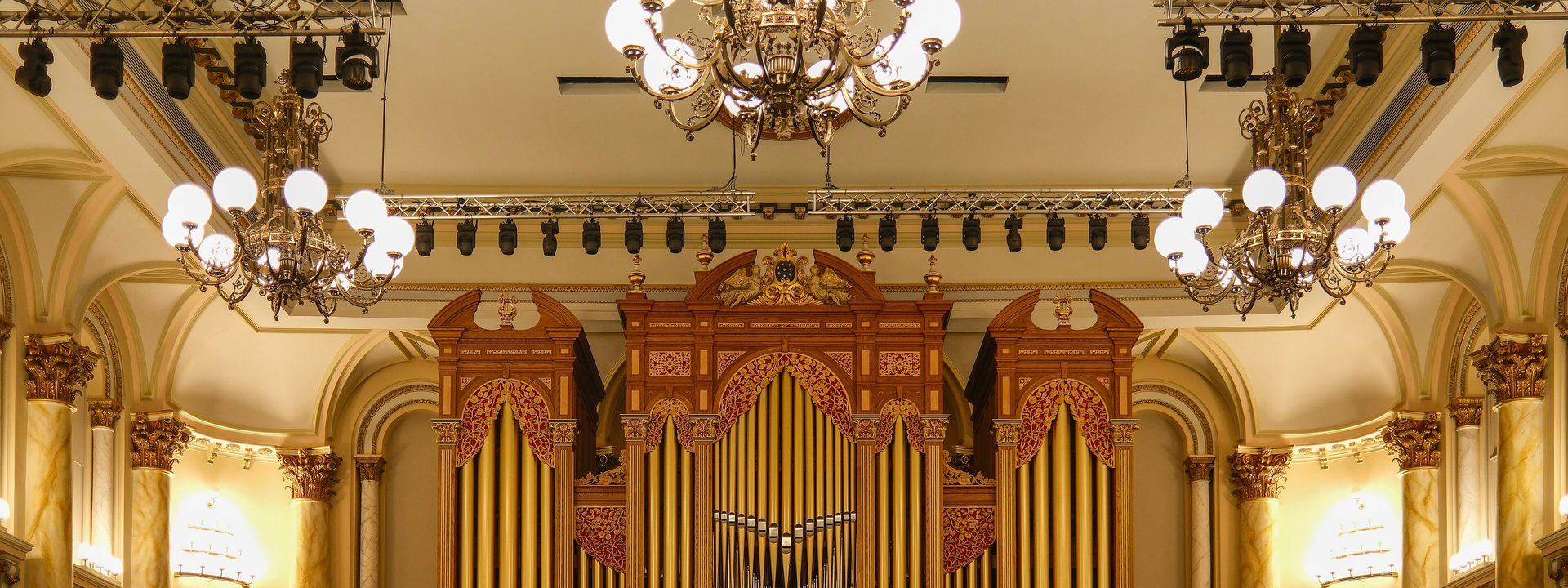 Adelaide Town Hall - A grand pipe organ with golden pipes dominates the ornate cream and gold interior of a classical concert hall.