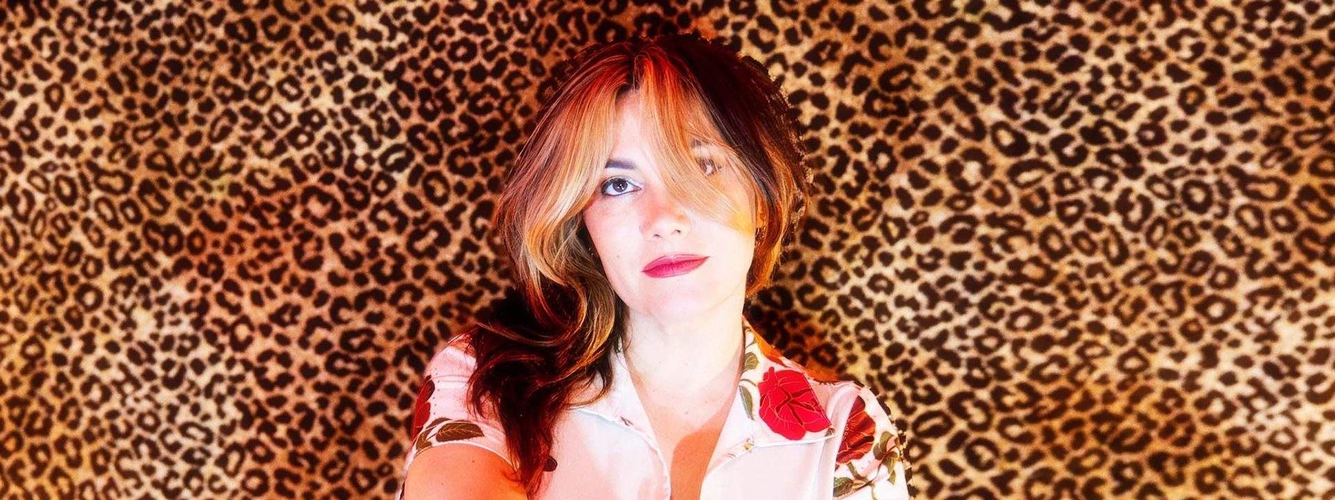 Person with reddish hair in a patterned shirt against a leopard print backdrop, gazing upward.
