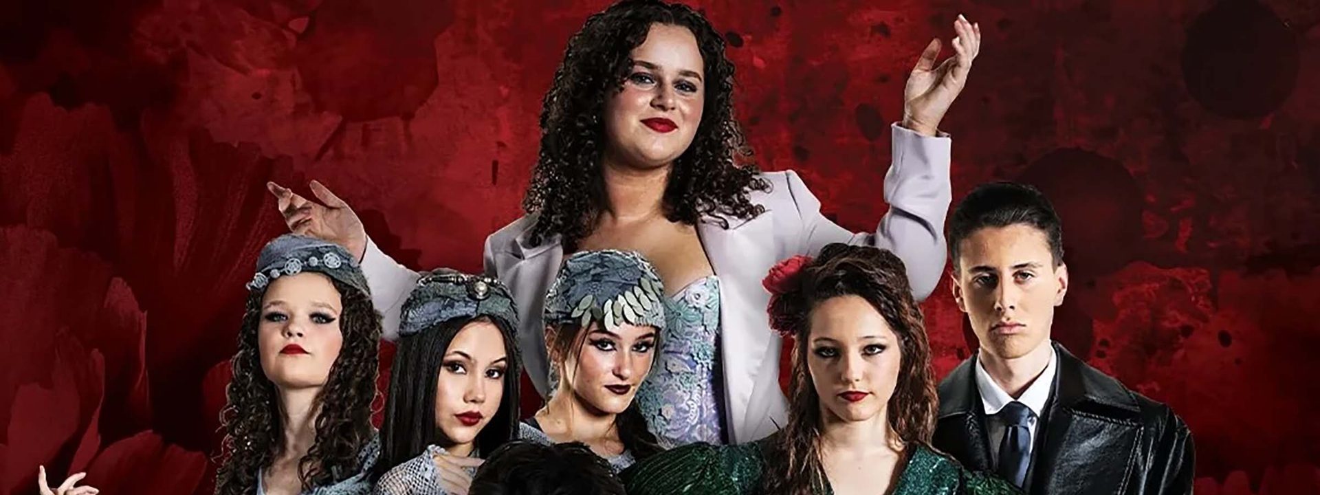 Group of eight performers in vintage-style costumes posed against a deep red textured backdrop.