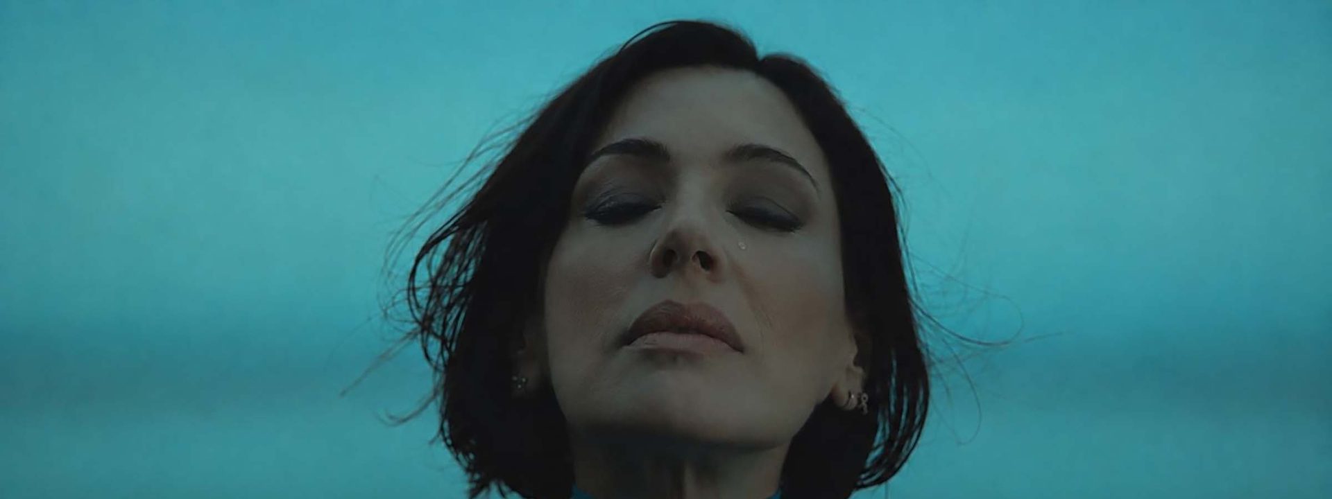 Woman with short dark hair gazes upward against a turquoise blue background.