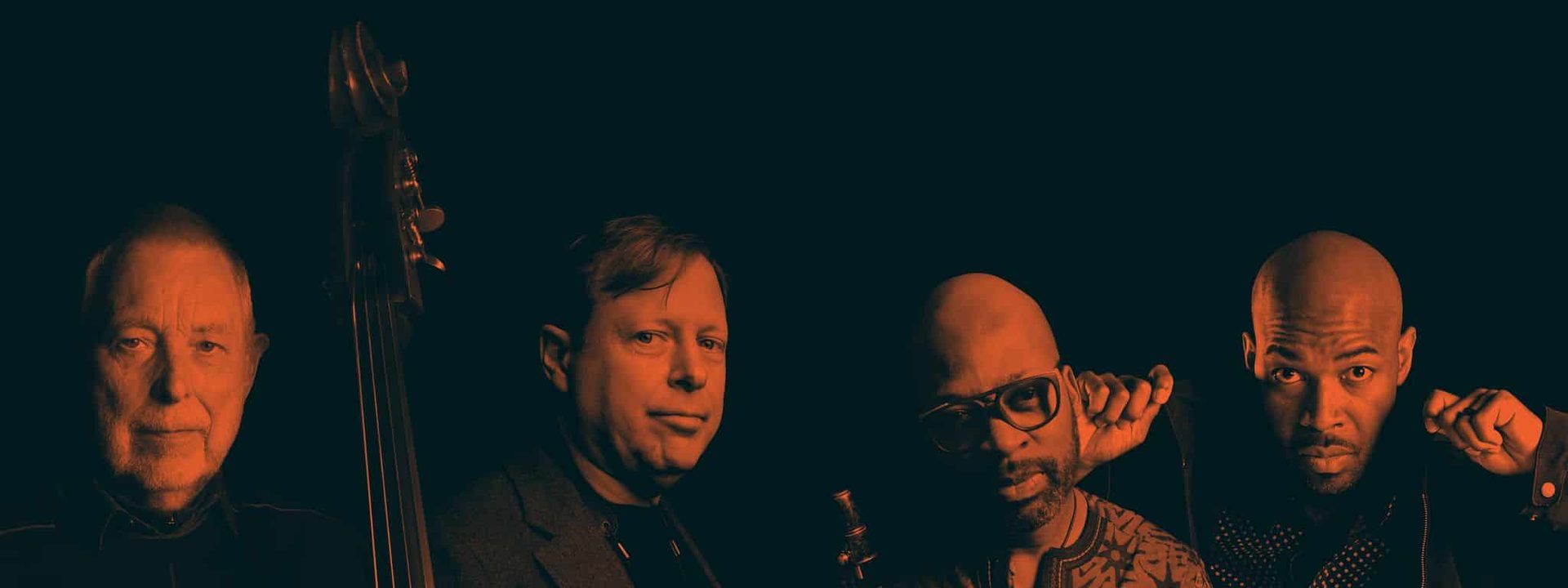 Five male musicians pose together holding instruments against a dark background.