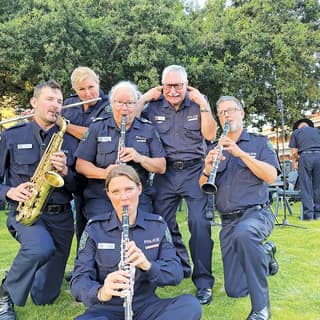 Concert - Six musicians in navy uniforms playing saxophone and woodwind instruments outdoors on a grass field.