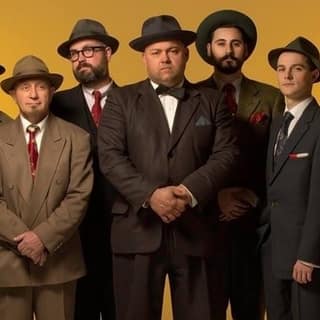 Harald's 92nd Birthday Celebration - Seven men in vintage suits and fedoras stand against a golden-yellow backdrop in formal poses.