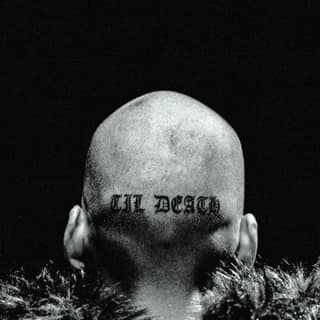 Club Angel - Shaved head with tattooed text viewed from behind against dark background, surrounded by wild grass.