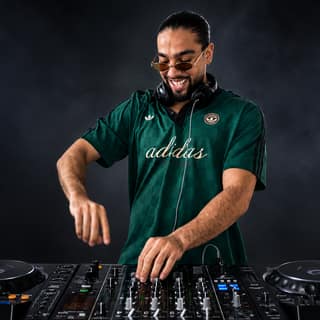 Adelaide's biggest nightlife experience lands at SORA with Amiks X The Joe and Zaffit Drummers - DJ in green shirt operating turntables under stage lighting at SORA nightclub.