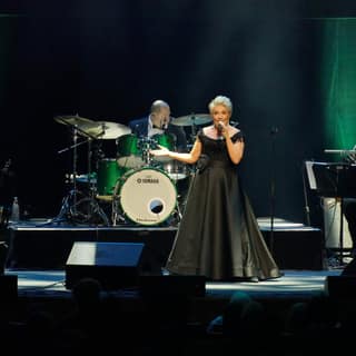 Melinda Schneider: The Way We Were - Female vocalist in a black dress performing centre stage with a live band under green theatrical lighting.