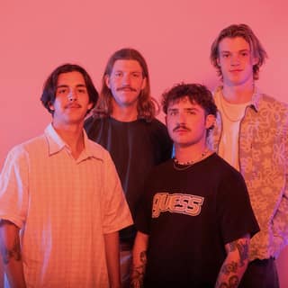 Four band members posed together against a pink-lit background for DICE.