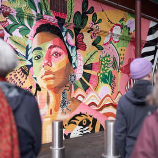 ,000 artists take over South Australia in August's SALA Festival - Gallery visitors view a vibrant portrait mural featuring a face painted in pink, green and yellow tones surrounded by botanical imagery.