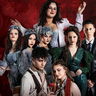 Group of eight performers in vintage-style costumes posed against a deep red textured backdrop.