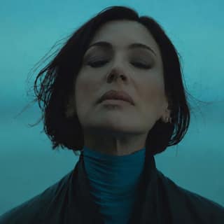 Woman with short dark hair gazes upward against a turquoise blue background.
