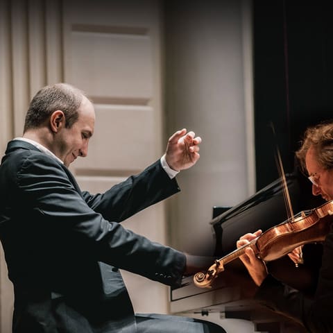 Richard Tognetti and Alexander Gavrylyuk - Violinist in dark jacket plays whilst conductor gestures expressively during a chamber performance at UKARIA.