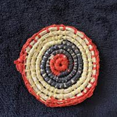 Circular woven textile with concentric rings in cream, red and dark blue, displayed flat against a dark background.
