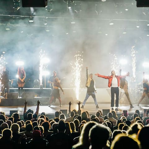 The King of Pop Show - Performers in red and white outfits dance on stage with pyrotechnics and dramatic lighting at Her Majesty's Theatre.