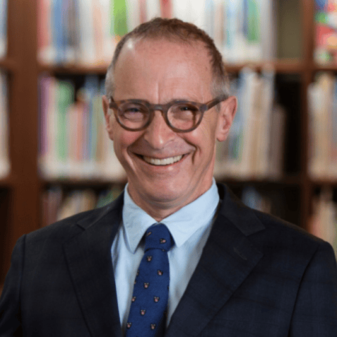 An Evening with David Sedaris - Man in glasses and dark blazer smiling in front of a bookshelf.