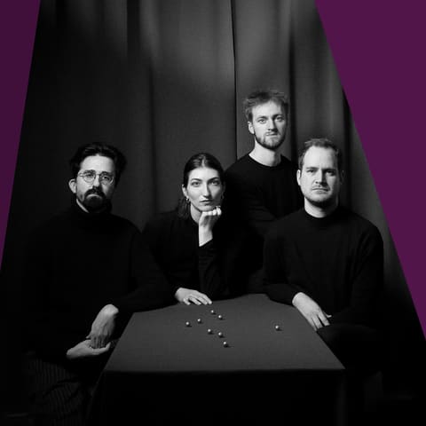 Chamberfest Concert Five | Full Flight – One Destination - Four musicians in black clothing posed around a table against a purple background.