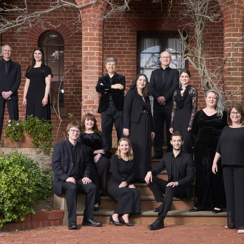 Adelaide Chamber Singers with Umberto Clerici and James Crabb - Choir members in black attire pose together outside a brick building with ivy.
