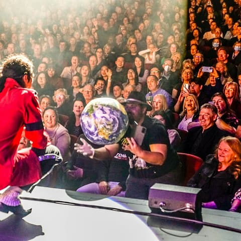 The King of Pop Show - Performer in red sequined jacket and white afro wig engages with audience members at Her Majesty's Theatre during The King of Pop Show.