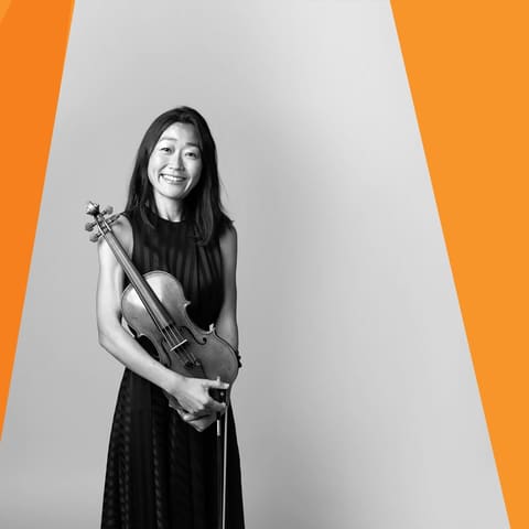 Chamberfest Concert Three | Kurtág 100 – Kafka Fragments - Violinist in black dress holding instrument against white and orange geometric background.