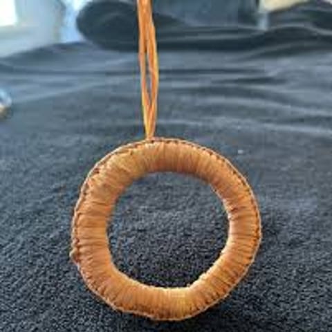 Woven circular ornament in golden-brown tones suspended by a thin cord.