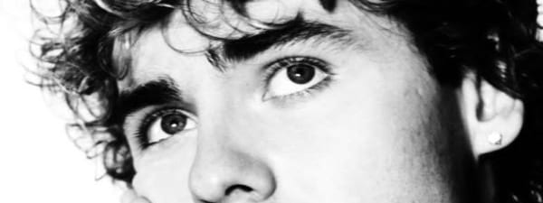 The long game pays off: Jack Gray's debut album arrives - Black and white portrait of a person with dark curly hair and hand raised thoughtfully to face against plain background.
