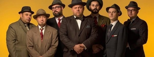 Harald's 92nd Birthday Celebration - Seven men in vintage suits and fedoras stand against a golden-yellow backdrop in formal poses.