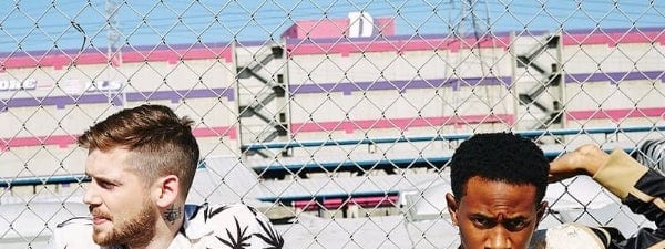 MKTO reunite Australian fans with first Adelaide date since 2012 breakthrough - Two musicians stand against a brick wall and chain-link fence beneath a pink and white striped building.