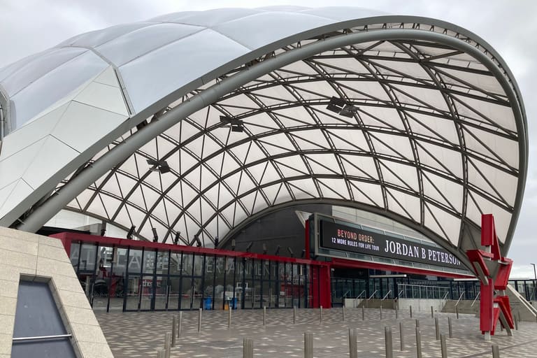 Adelaide Entertainment Centre - Modern curved building with geometric lattice roof structure and red entrance facade beneath overcast sky.