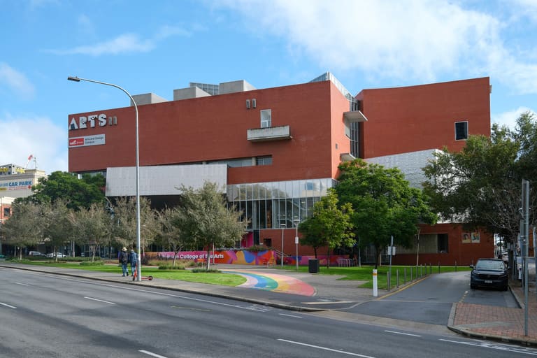 Adelaide College of the Arts - A modern red brick arts building with white sections sits on a corner street with green landscaping and street lamp.