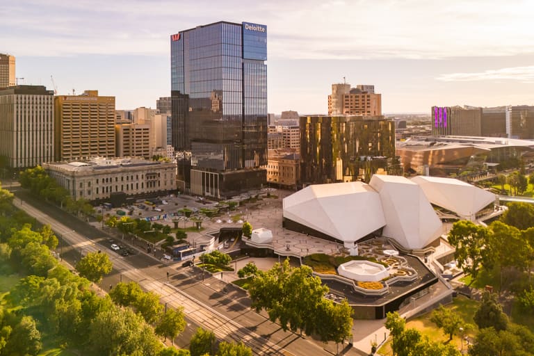 Adelaide Festival Theatre - Modern white building with curved architecture sits among tall urban skyscrapers in a city centre.