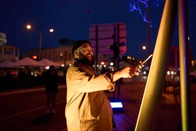 Person in yellow jacket interacting with illuminated public art installation at dusk during SALA Festival.