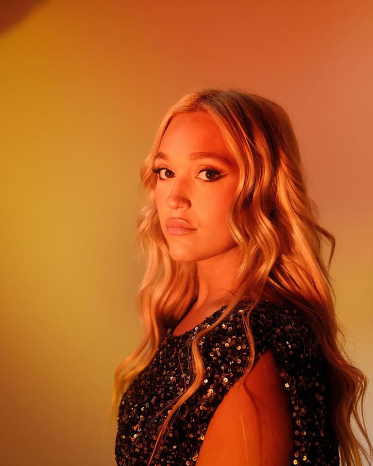 IVANA remakes Jennifer Paige and Cascada for the dancefloor - Performer with long blonde hair in a sequined black jacket against warm orange and yellow stage lighting.
