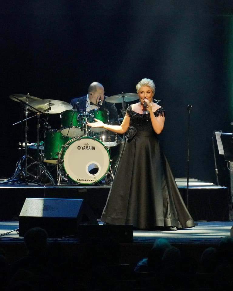 Melinda Schneider: The Way We Were - Female vocalist in a black dress performing centre stage with a live band under green theatrical lighting.