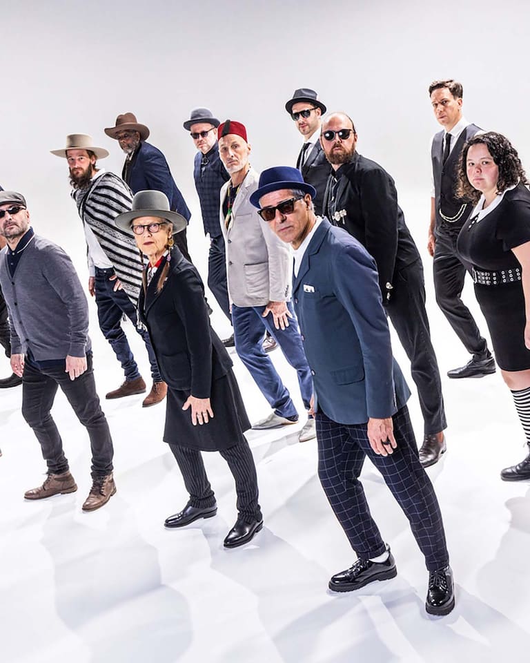 Large group of people in casual and formal attire standing together against a white background.