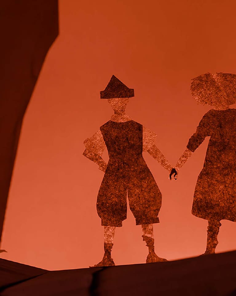 Two silhouetted figures in period costume stand together against a warm orange backdrop in a stylised theatrical scene.