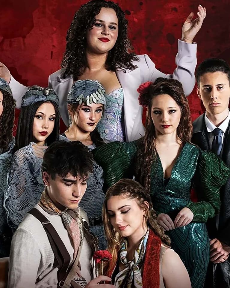 Group of eight performers in vintage-style costumes posed against a deep red textured backdrop.