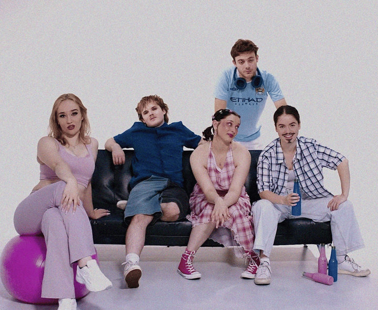 Five performers posed on a bench against a grey backdrop, wearing casual clothing in pastel and neutral tones.