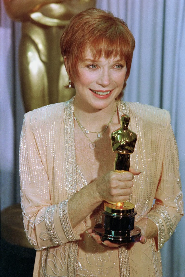 Woman with short reddish hair holding a gold Academy Award statuette, wearing a beige sequined jacket.