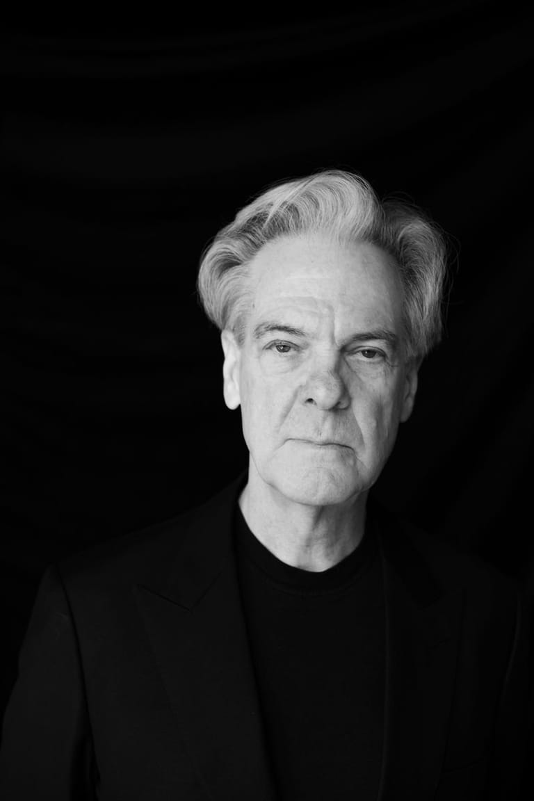 Black and white portrait of a man with grey hair against a dark background.