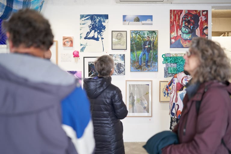 Gallery visitors viewing an eclectic collection of artworks displayed on a white gallery wall.