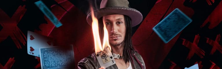 Performer in a grey hat and jacket surrounded by floating playing cards against a red and blue backdrop.