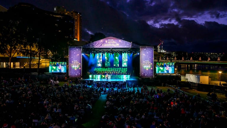 Large outdoor concert stage illuminated in blue and purple lights with crowd gathered at night.