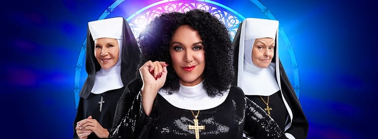 Woman in nun costume with curly dark hair flanked by two figures in traditional habits against blue and purple stage lighting.