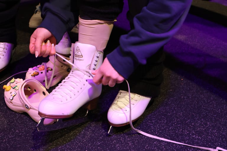 Pink roller skate being laced up under purple stage lighting during a performance.