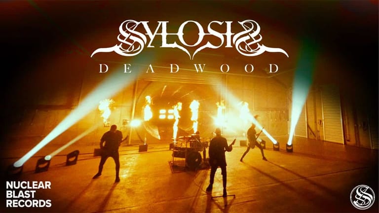 Band members silhouetted against golden stage lighting and flames during a Sylosis performance.
