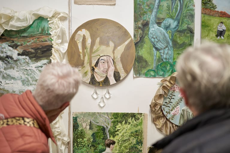 Two visitors view an exhibition of nature-inspired artworks including circular and rectangular pieces on a white wall.