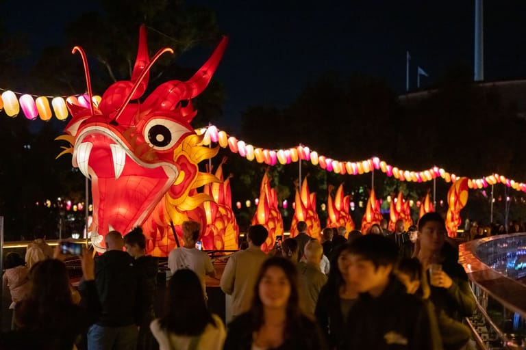 Illuminated red and gold lantern dragon sculpture surrounded by crowds at night-time festival celebration.